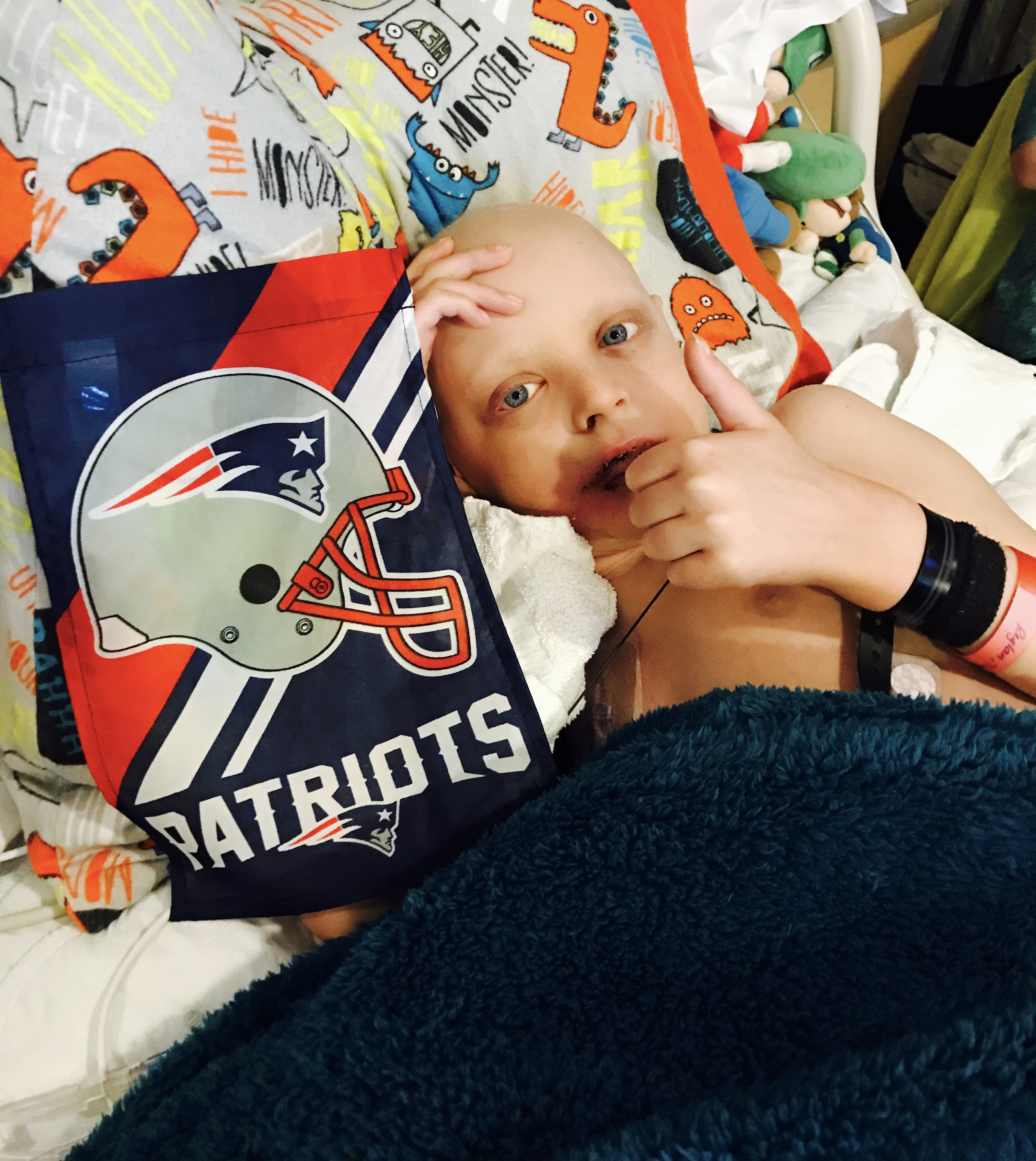 Max making a faint smile and thumbs up sign next to a Patriots football flag